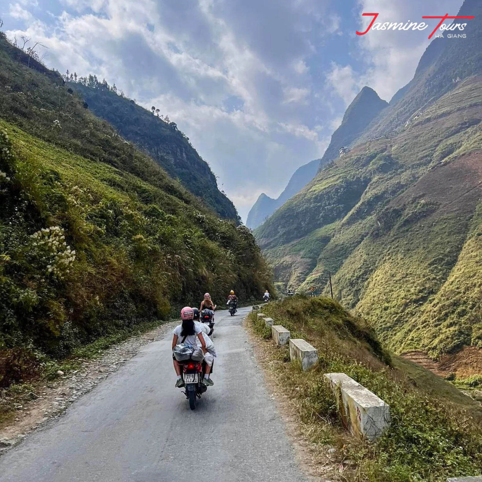 Riders on the Ha Giang Loop on a narrow sealed mountain road with concrete crash barriers, limestone peaks rising on both sides