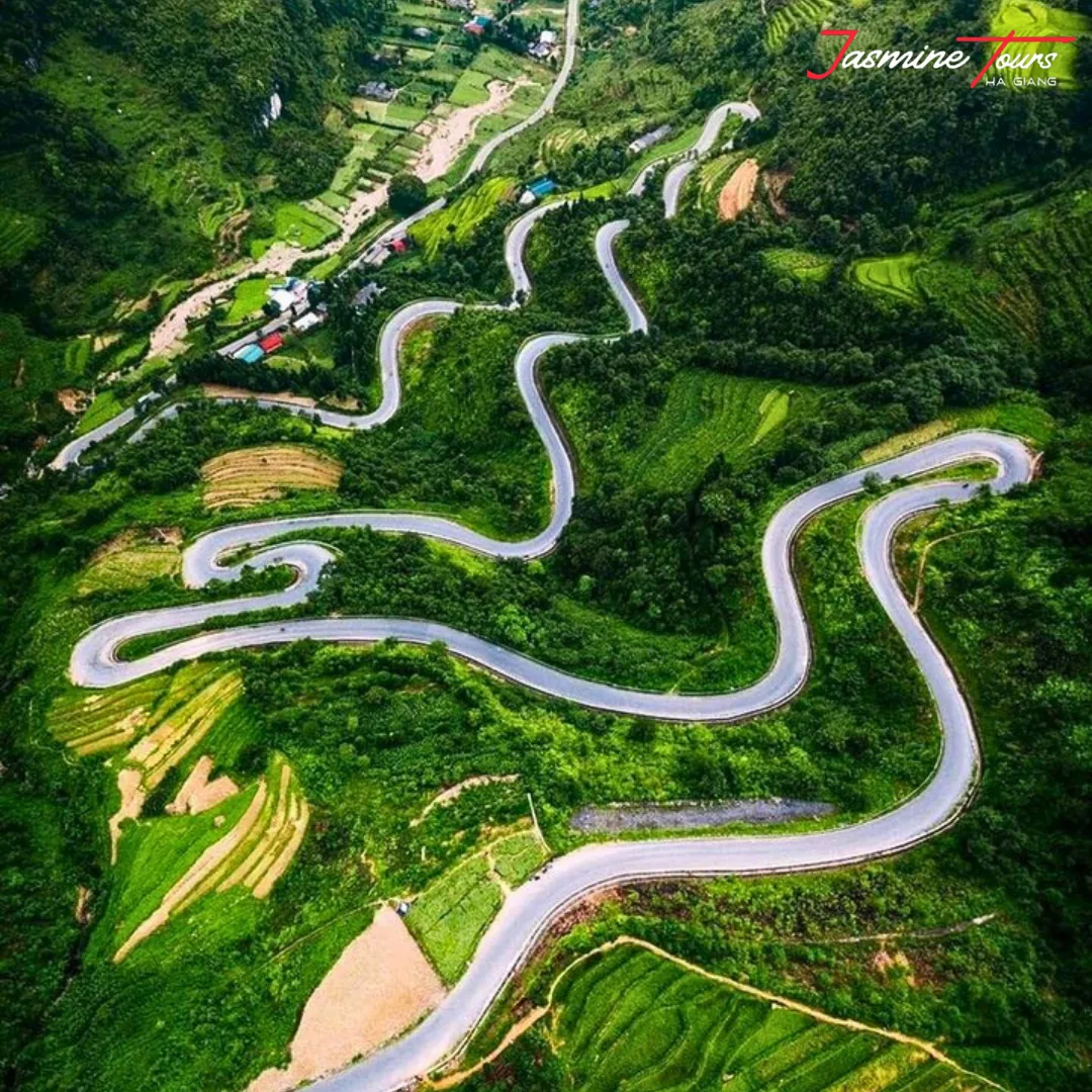Aerial view of stacked switchbacks on a Ha Giang Loop road in clear weather, cutting through bright green terraced hillsides