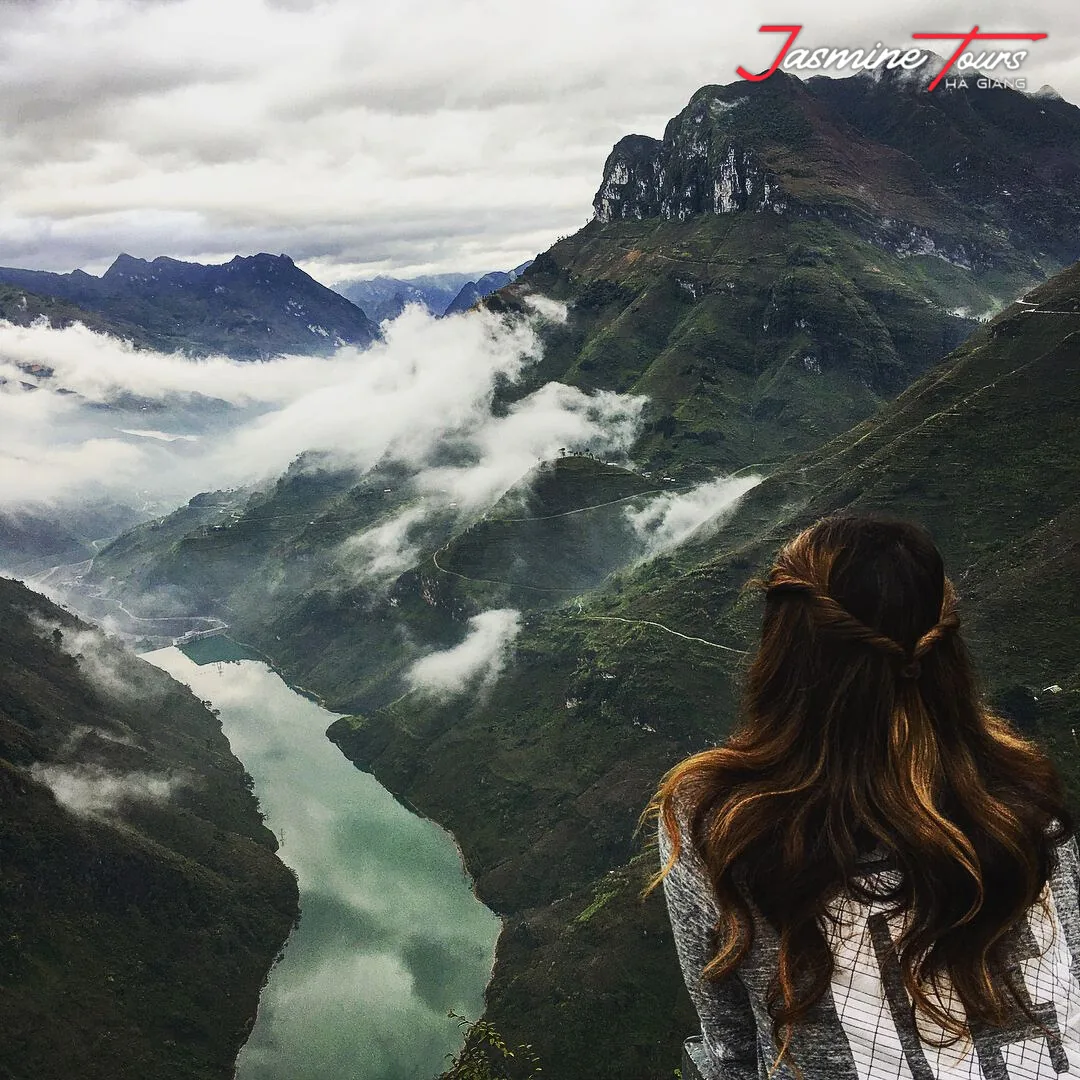 Cloud pouring over a ridge above the Nho Quế river gorge on the Ha Giang Loop, with a viewer looking down at the water from a high viewpoint