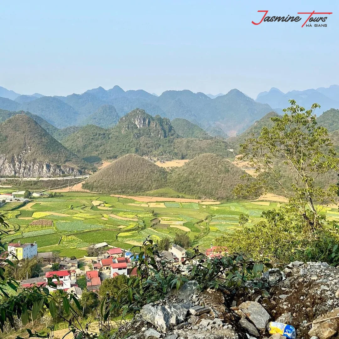 A wide karst valley in northern Vietnam with cultivated fields, a village of red-roofed houses and limestone peaks receding into haze