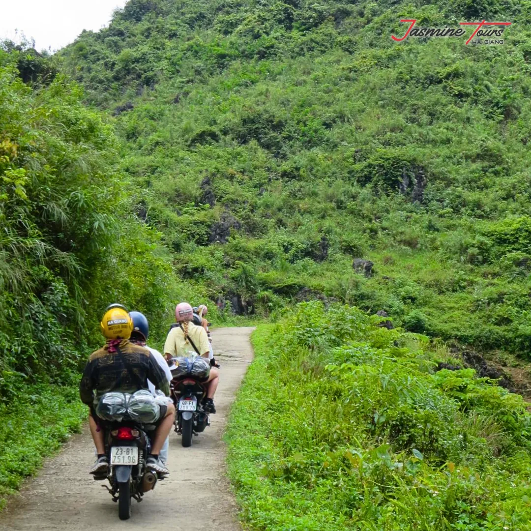 Two motorbikes riding away from the camera on a narrow concrete track between steep green karst slopes on the Ha Giang Loop