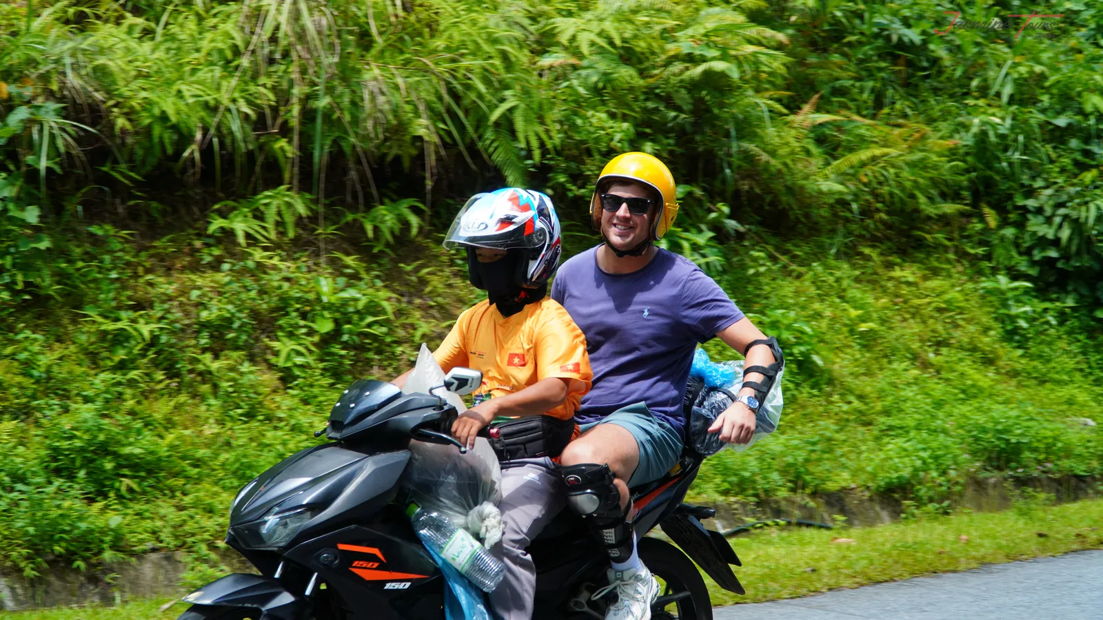 A local driver in an orange jersey and a guest sitting together on a motorbike at the roadside in Ha Giang.