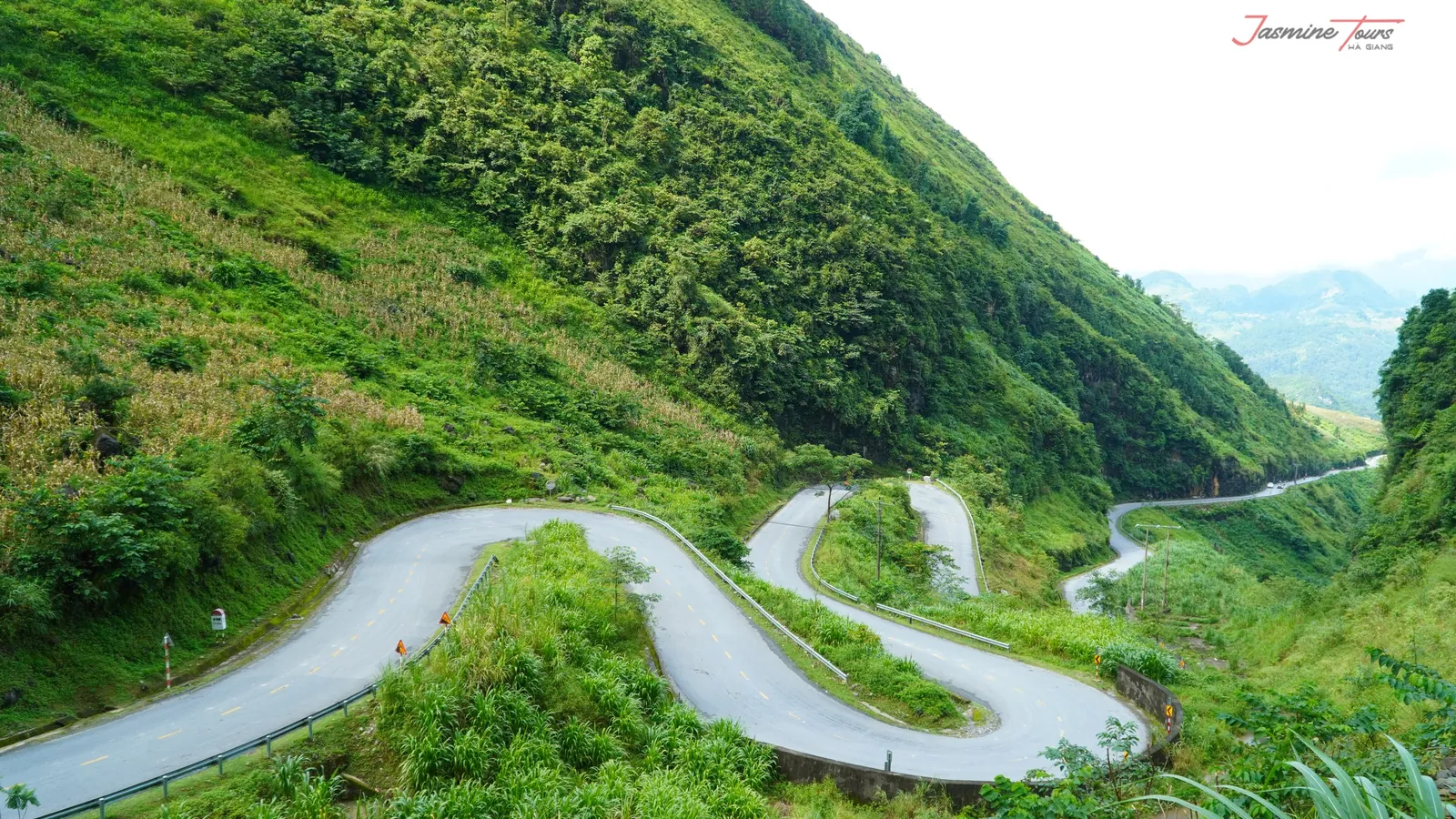 Three empty switchbacks descending a green mountainside in Ha Giang, with no vehicle on the road.