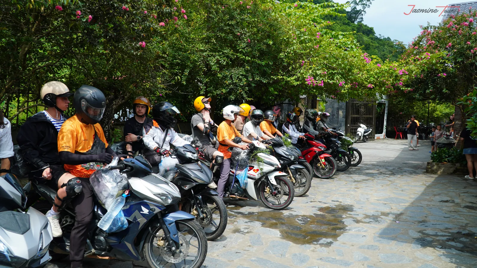 A line of parked motorbikes with riders in helmets waiting on a wet lane before setting off in Ha Giang.