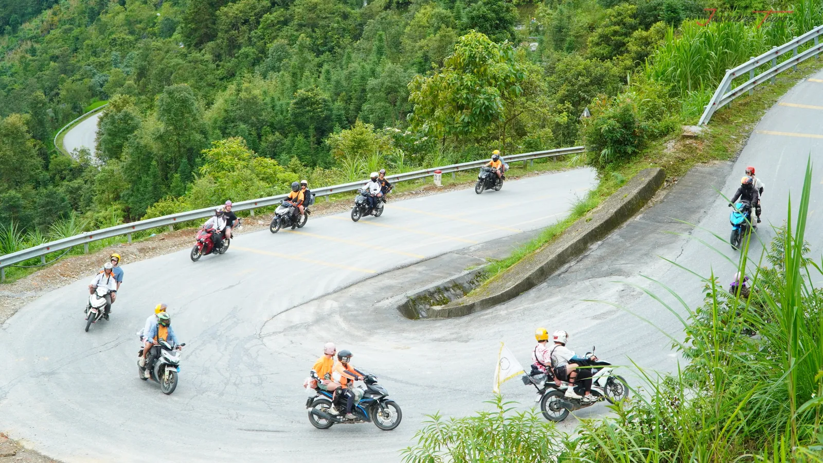 More than ten motorbikes carrying riders around a single hairpin bend on a mountain road in Ha Giang, the riders wearing several different companies' jerseys and helmet colours.
